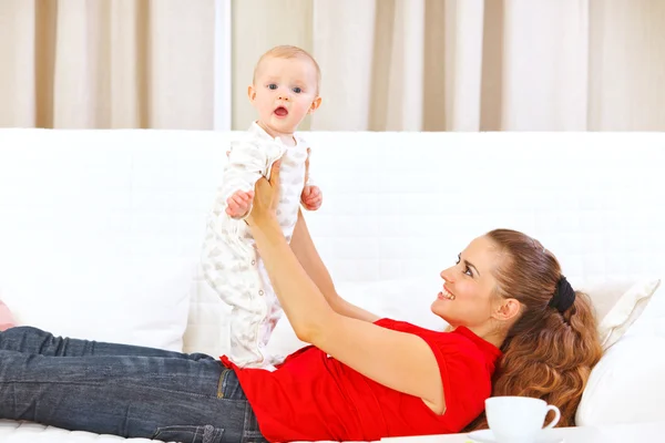 Sorridente madre e adorabile bambino che gioca sul divano — Foto Stock