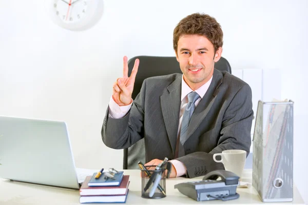 Sorrindo homem de negócios moderno sentado na mesa de escritório e mostrando vi — Fotografia de Stock