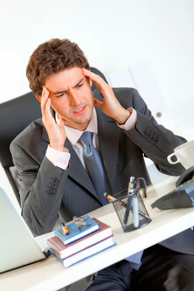 Бизнесмен с головной болью сидит за рабочим столом и держится за руки во главе — стоковое фото