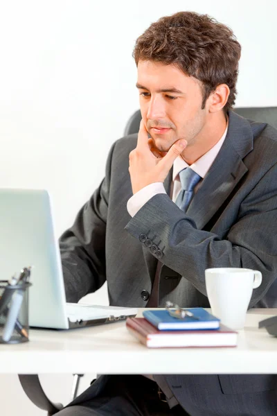 Un uomo d'affari premuroso seduto alla scrivania dell'ufficio e che lavora sul computer portatile — Foto Stock