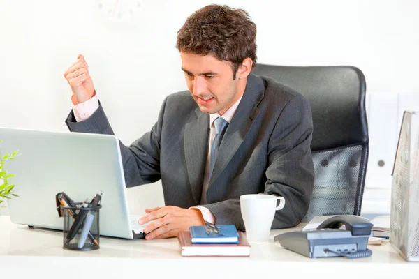 Wütender Geschäftsmann sitzt am Schreibtisch und schwenkt bedrohlich sein Handy — Stockfoto