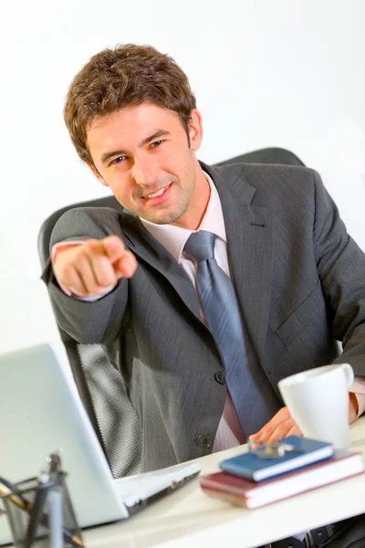 Sorrindo homem de negócios moderno sentado na mesa de escritório e apontando o — Fotografia de Stock