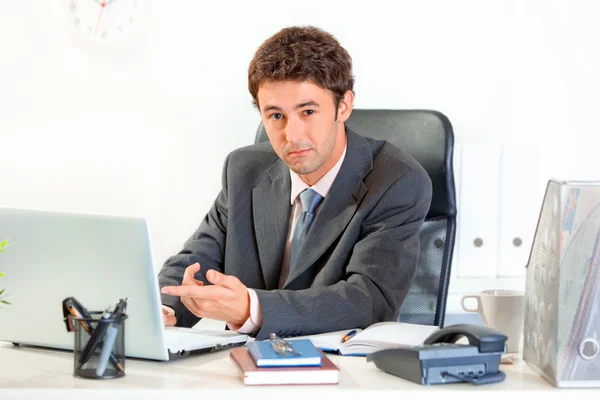 Modern businessman sitting at office desk and pointing finger on laptop — Stock Photo, Image