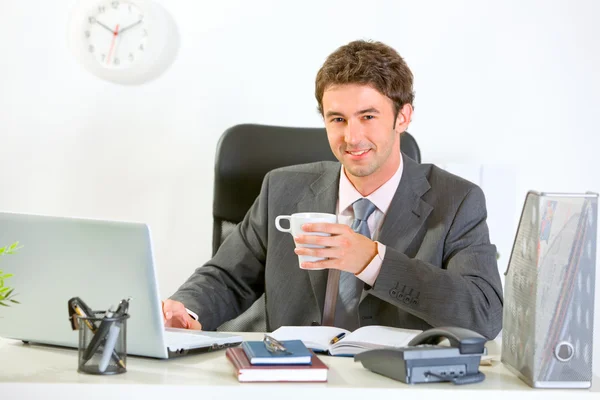 モダンな実業家のオフィスの机に座って、コーヒーを飲んでいます。 — ストック写真
