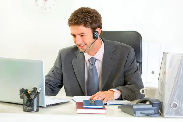 Sorrindo gerente moderno com fone de ouvido olhando no laptop — Fotografia de Stock