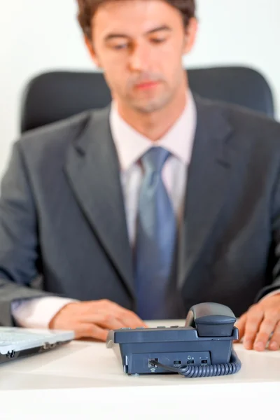 Hombre de negocios sentado en el escritorio de la oficina y esperando una llamada telefónica. Concéntrate en teléfono — Foto de Stock