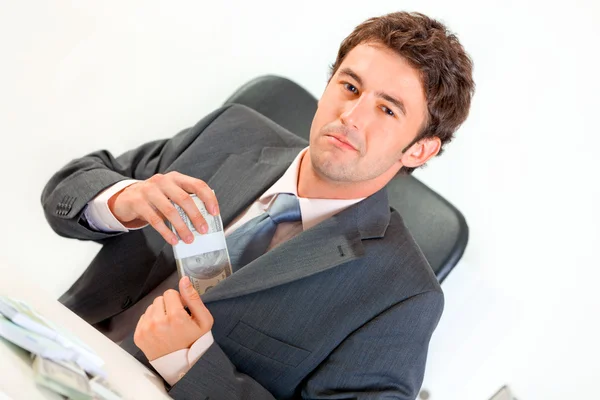 Confident businessman sitting at office desk and putting money in pocket — Stock Photo, Image