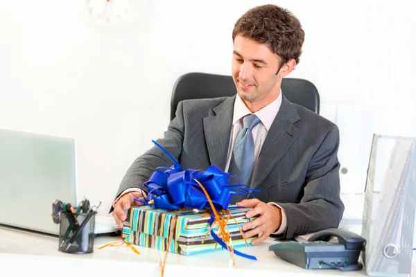 stock image Pleased businessman sitting at office desk and looking on gift