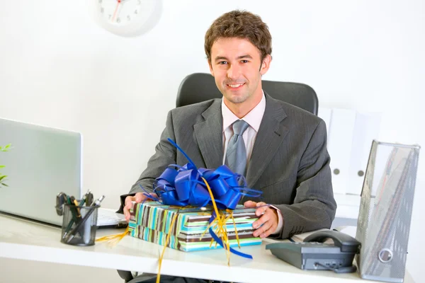 Happy businessman sitting with gift at office desk — Stock Photo, Image