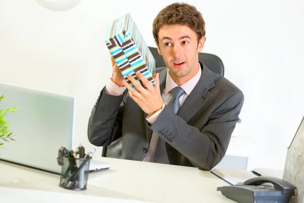 Цікавий бізнесмен струшуючи подарункову коробку, намагаючись вгадати, що — стокове фото
