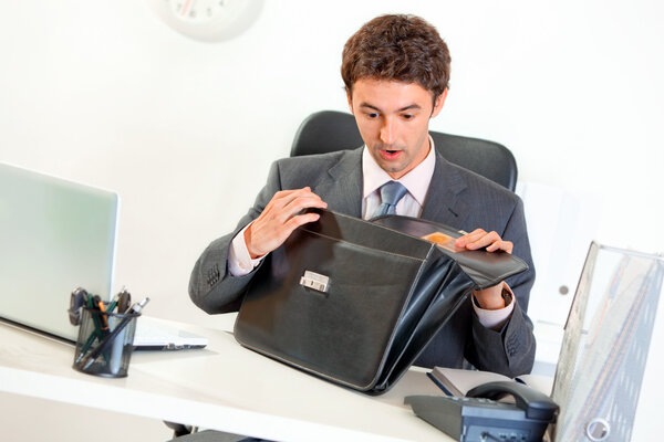 Shocked businessman sitting at office desk and looking in briefcase