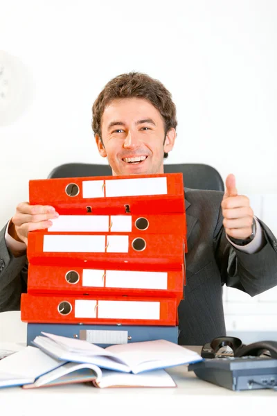 Siedząc przy biurku urząd uśmiechający się biznesmen patrząc od stos folderów — Zdjęcie stockowe