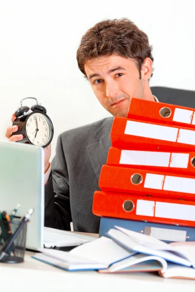 Missnöjd affärsman sitter på skrivbord med högen av mappar och ho — Stockfoto