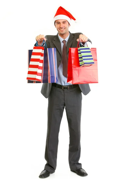 Smiling businessman in Santa hat giving shopping bags — Stock Photo, Image