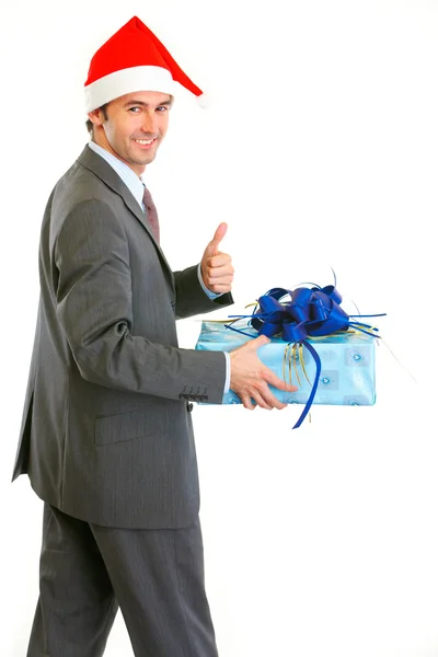 Empresário moderno feliz em Santa Hat segurando presente e showin — Fotografia de Stock