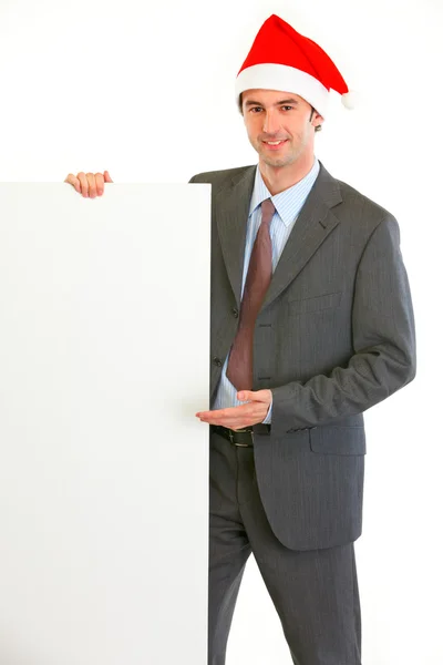 Sonriente hombre de negocios moderno en Santa Hat mostrando cartelera en blanco —  Fotos de Stock