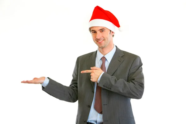 Smiling modern businessman in Santa Hat pointing on empty hand — Stock Photo, Image