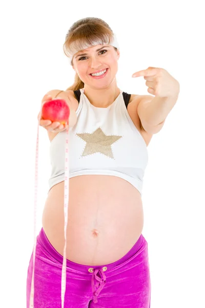 Sorridente bella donna incinta che punta il dito al nastro di misura e mela — Foto Stock