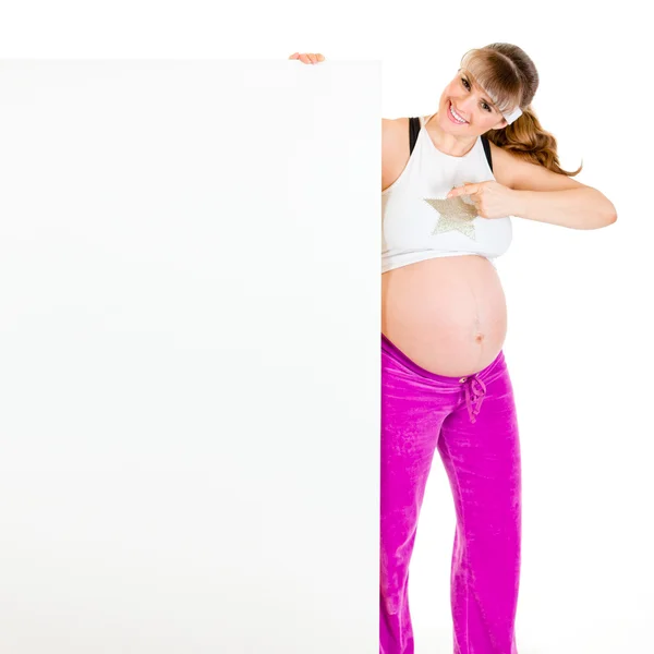 Усміхнена красива вагітна жінка вказує пальцем на порожній рекламний щит — стокове фото