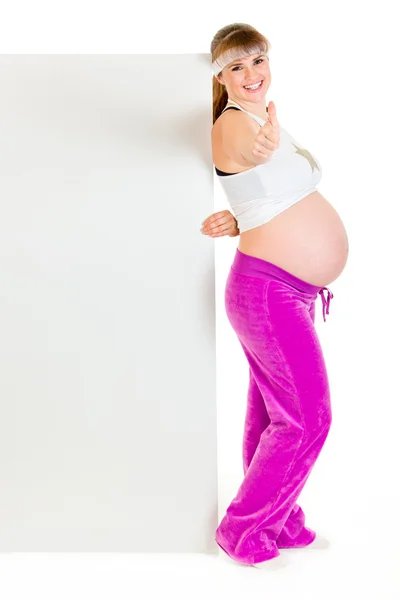 Sonriendo hermosa mujer embarazada sosteniendo la cartelera en blanco y mostrando pulgares — Foto de Stock