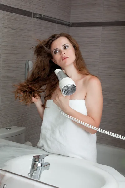 Привлекательная женщина использует фен в ванной комнате — стоковое фото