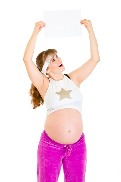 Sorprendida hermosa embarazada sosteniendo papel blanco vacío sobre su cabeza —  Fotos de Stock