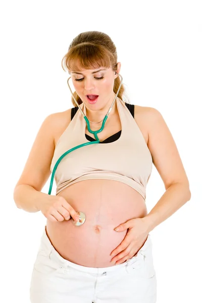 Удивлённая беременная женщина держит стетаскоп на животе — стоковое фото