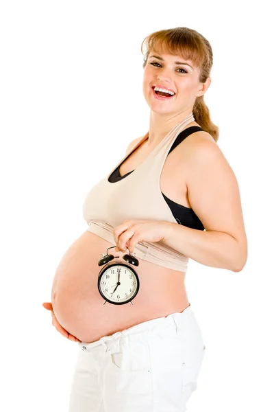 Mulher grávida feliz segurando despertador na frente de sua barriga — Fotografia de Stock