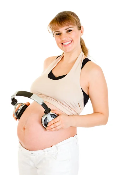 Usmívající se těhotná žena drží sluchátka na břiše — Stock fotografie