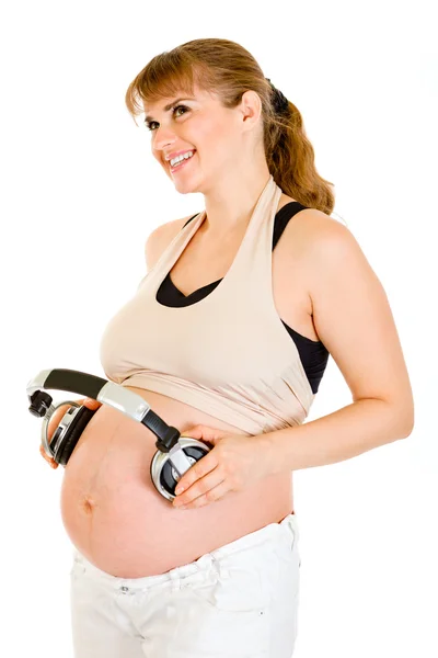 Ευτυχής έγκυος γυναίκα που κρατά ακουστικά την κοιλίτσα της — Φωτογραφία Αρχείου