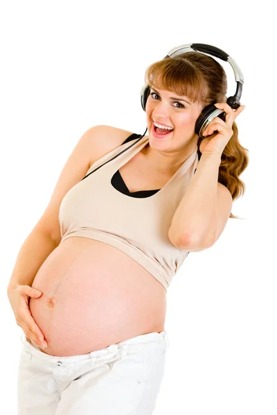 Улыбающаяся беременная женщина держит живот и слушает музыку в наушниках — стоковое фото