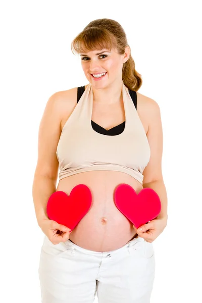 Kobieta w ciąży uśmiechający się gospodarstwa papieru serca w pobliżu jej brzuch — Zdjęcie stockowe