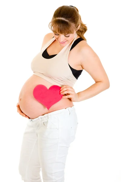 Mujer embarazada sonriente sosteniendo el corazón cerca de su barriga — Foto de Stock