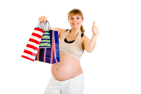 Feliz embarazada sosteniendo bolsas de la compra y mostrando los pulgares hacia arriba gesto —  Fotos de Stock