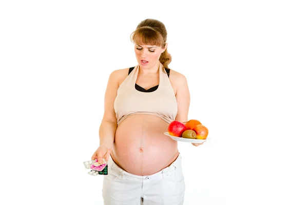 Düşünceli hamile kadın hapları ve meyveler arasında seçim yapma — Stok fotoğraf