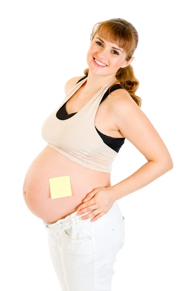 Mujer embarazada sonriente con una nota adhesiva en blanco en su vientre — Foto de Stock