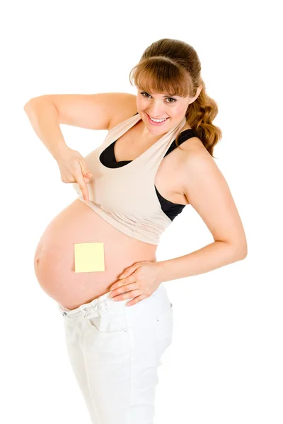 Lachende zwangere woman wijzend op lege notitie op haar buik — Stockfoto