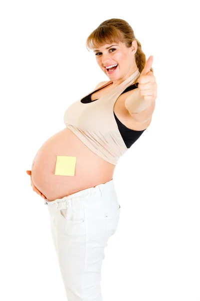 Mujer embarazada sonriente con nota adhesiva en blanco en su vientre mostrando pulgares u —  Fotos de Stock
