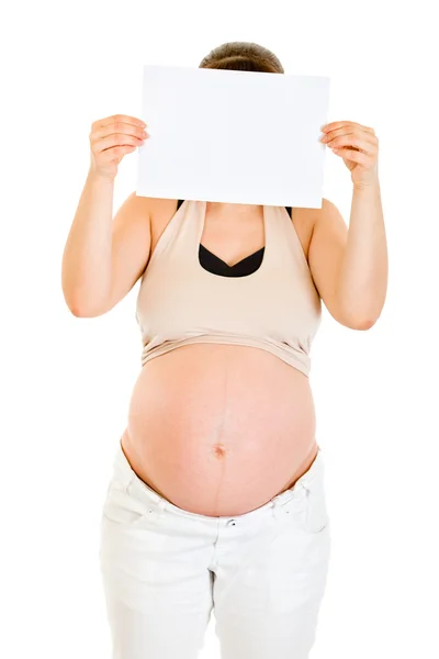 Mulher grávida segurando papel branco vazio na frente de seu rosto — Fotografia de Stock