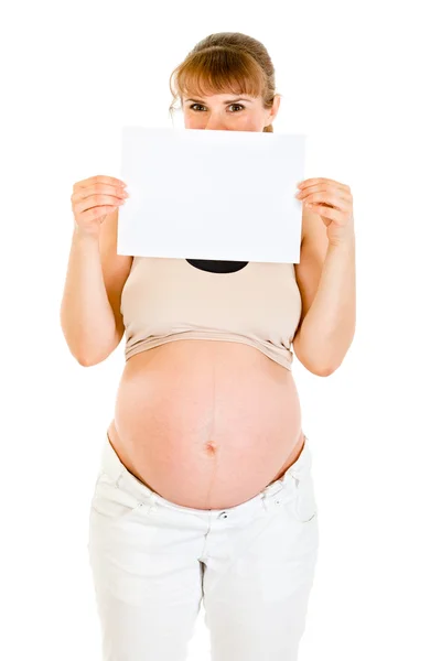 Mujer embarazada sosteniendo papel blanco vacío delante de su cara — Foto de Stock