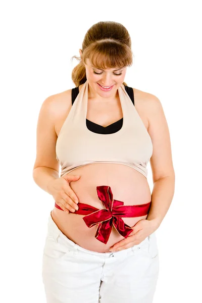 Smiling beautiful pregnant woman holding her belly with red ribbon on it — Stock Photo, Image