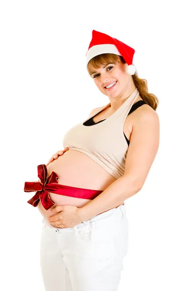 Szczęśliwy piękne kobiety w ciąży w santa hat z czerwoną wstążką na brzuch — Zdjęcie stockowe