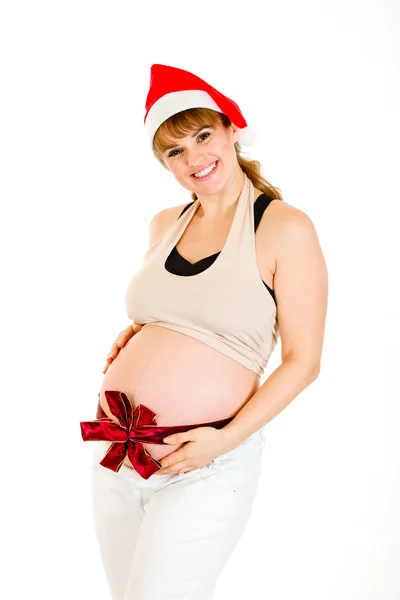 サンタの帽子を腹に赤いリボンで幸せなクリスマスの妊娠中の女性 — ストック写真