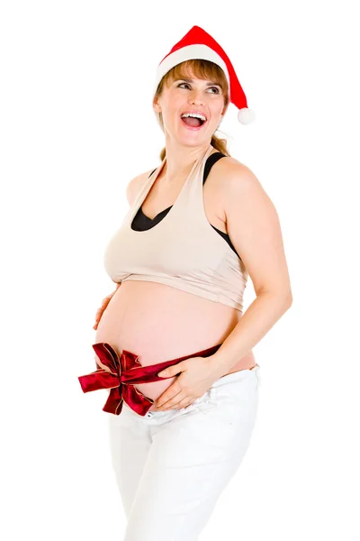 Zadowolony Boże Narodzenie ciąży kobieta w santa hat z czerwoną wstążką na brzuch — Zdjęcie stockowe