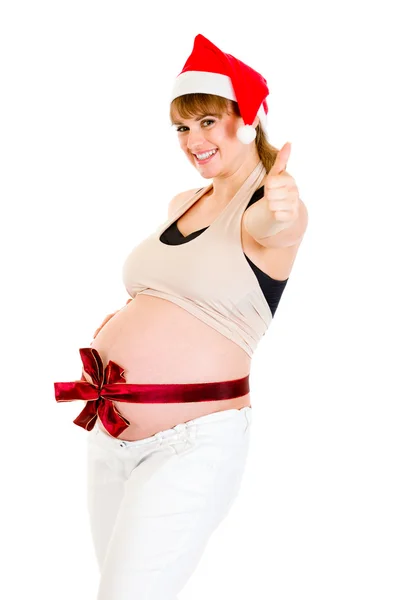 サンタの帽子を示すジェスチャーを親指で幸せなクリスマスの妊娠中の女性 — ストック写真
