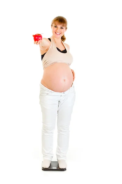 Улыбающаяся беременная женщина, стоящая на весах и держащая яблоко в руке — стоковое фото