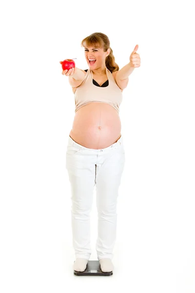 Удовлетворенная беременная женщина, стоящая на весах и показывающая большие пальцы — стоковое фото