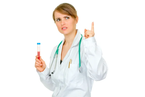 Nachdenkliche Ärztin mit erhobenem Finger, der Reagenzgläser hält — Stockfoto