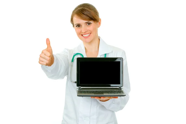 Doctora mujer sosteniendo portátil con pantalla en blanco y mostrando los pulgares hacia arriba gesto —  Fotos de Stock