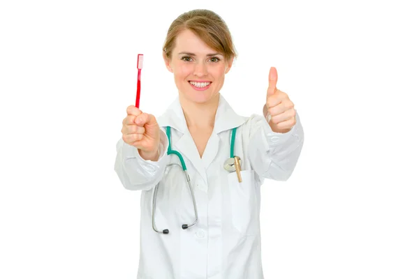 Uśmiechnięta kobieta dentysty trzymając szczoteczkę do zębów i pokazano kciuki gest — Zdjęcie stockowe